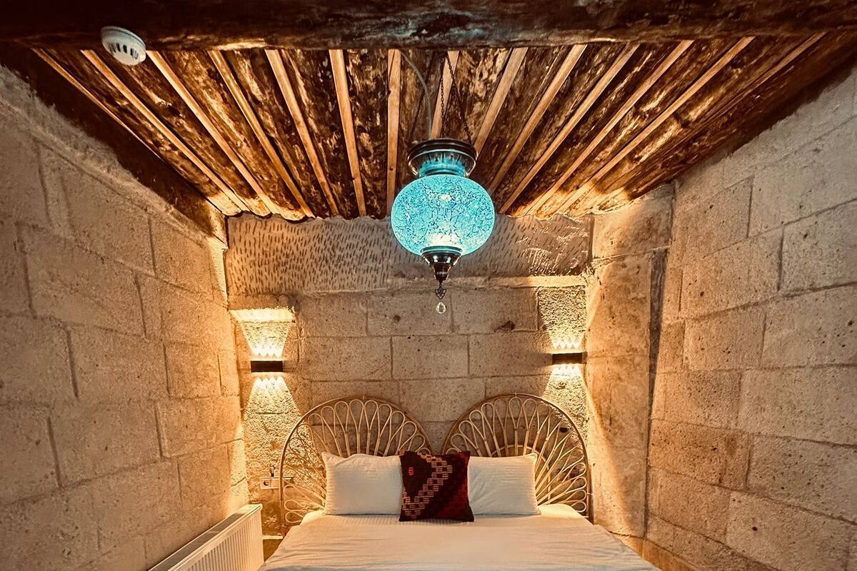 A cozy bedroom with a wooden ceiling, a large bed with a red bedspread, and a unique blue lamp.