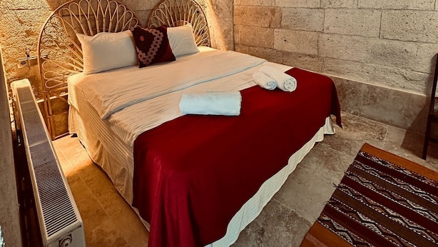 Una camera da letto con soffitto in legno, un letto con coperta rossa, cuscino bianco e tappeto a motivi.