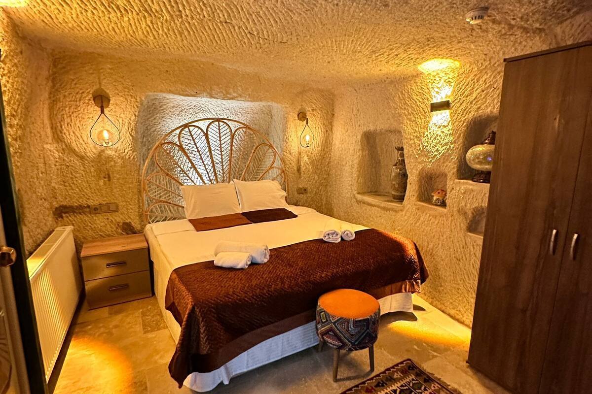 A cozy, stone-walled bedroom with a bed, bedside tables, a wardrobe, and a patterned rug.