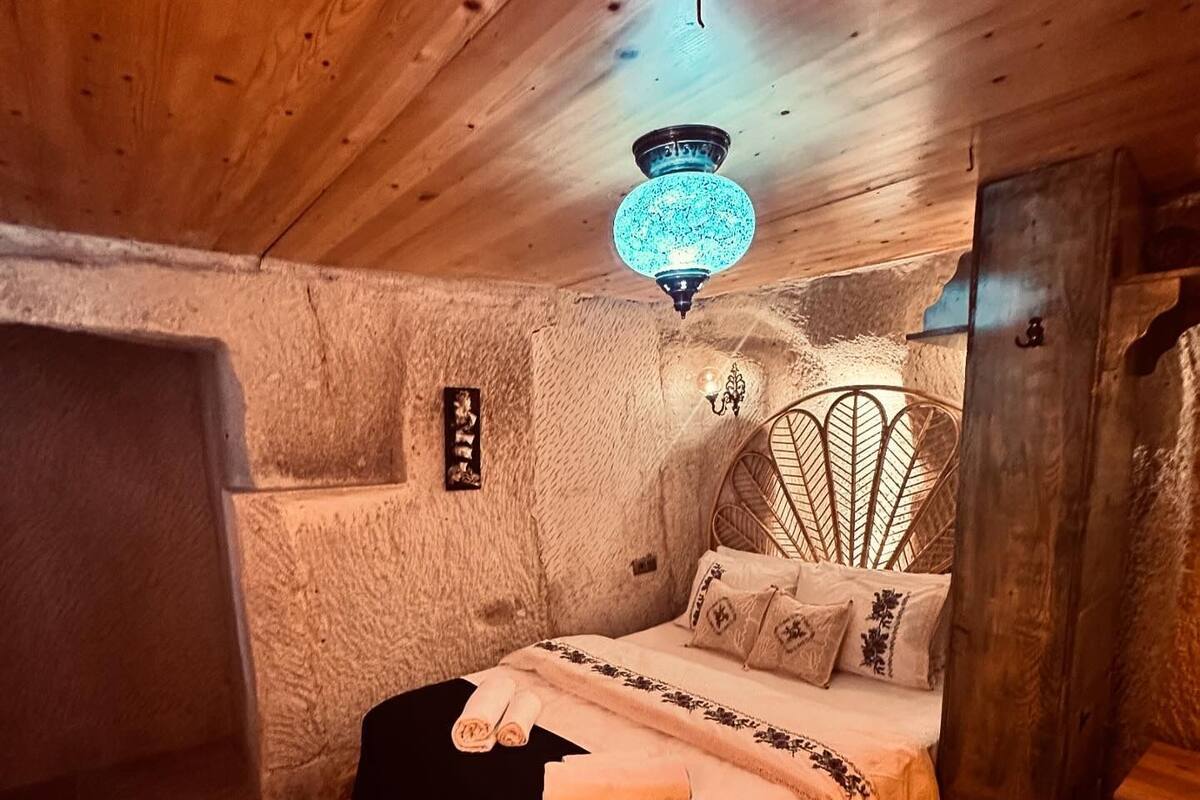 A cozy, rustic room with a wooden ceiling, a bed with a patterned bedspread, a small round table, and a decorative wall piece.