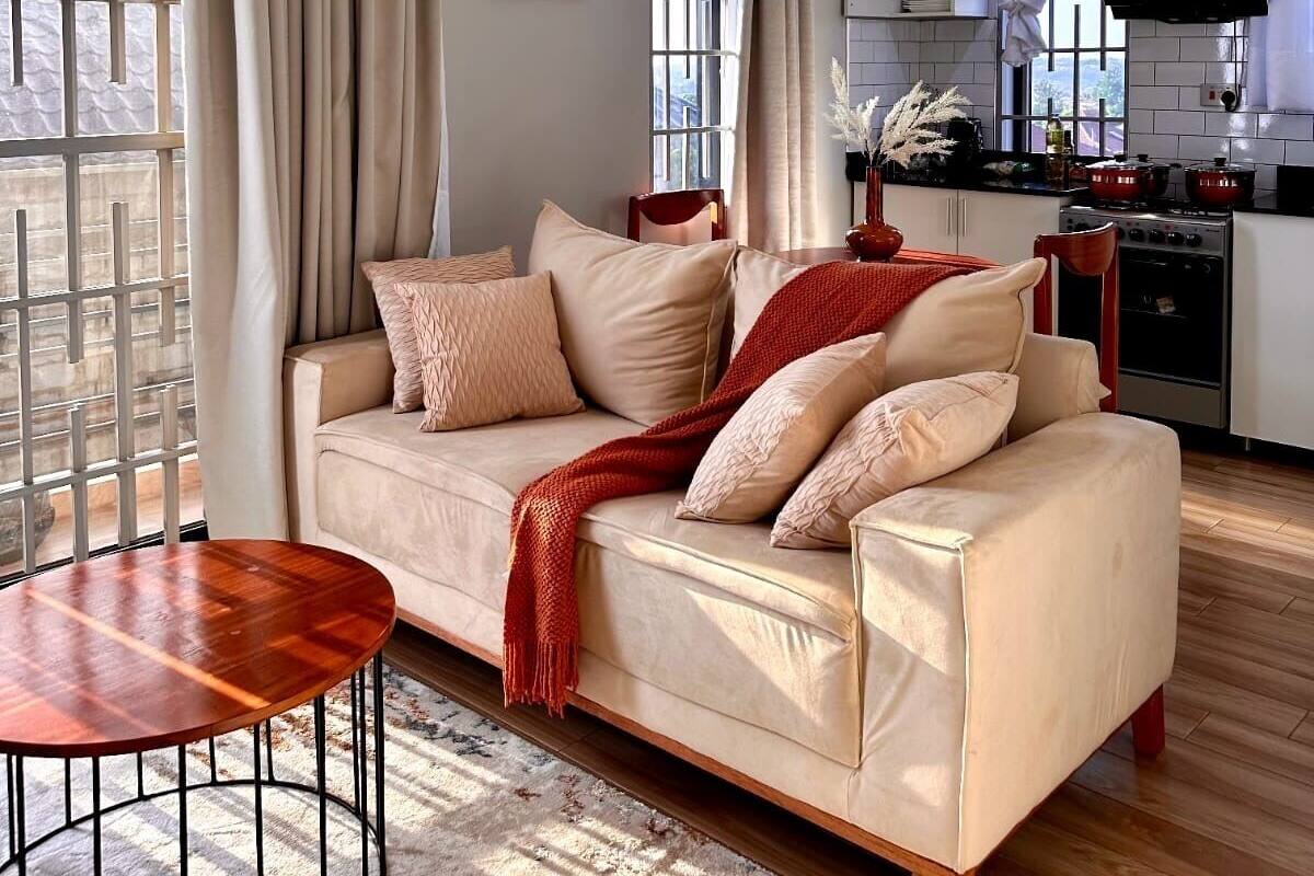 Een moderne woonkamer met een beige bank, een ronde houten tafel en een groot raam met gordijnen.