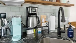 A kitchen with a coffee maker, a kettle, a bottle of hand soap, and a jar of utensils.