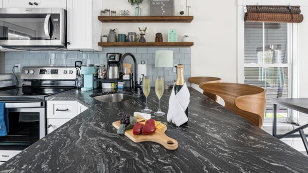 A modern kitchen with a marble countertop, stainless steel appliances, and a wooden dining area.