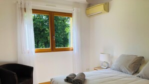 Habitación de hotel con cama, una silla, mesita de noche con lámpara y ventana con cortinas.