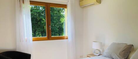 A hotel room with a bed, a chair, a bedside table with a lamp, and a window with curtains.