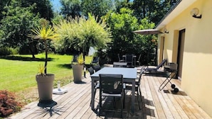Un patio al aire libre con una mesa y sillas, rodeado de plantas en macetas y vistas a un área con césped.