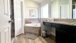 Ein modernes Badezimmer mit Holzboden, einer Badewanne, einem Waschtisch mit Spiegel und einem Handtuchhalter.