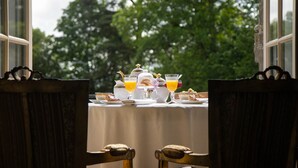 A table set for breakfast with tea, coffee, and orange juice, overlooking a garden. - Château Bagen (SAUVETERRE DE COMMINGES)