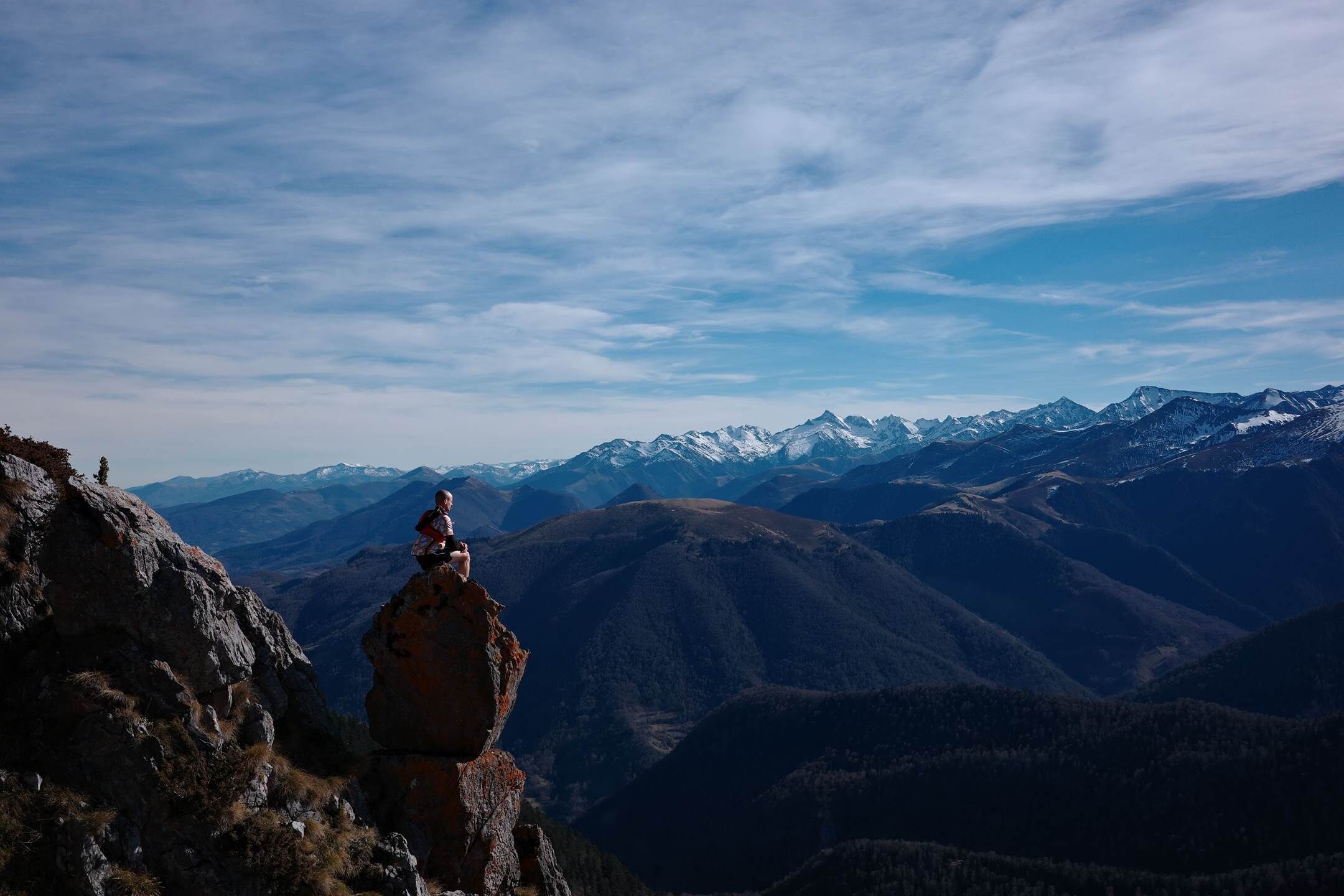 A person standing on a rock formation with a view of snow-capped mountains in the background.