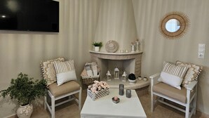 A cozy living room with a fireplace, two armchairs, a coffee table, and a TV mounted on the wall. - Ornament:Infinite Nature Villa
Feel Nature, Enjoy Serenity, Live THE Experience! (Heraklion)