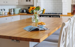 A kitchen with a wooden countertop, a vase with sunflowers, a bowl of chips, and a magazine.