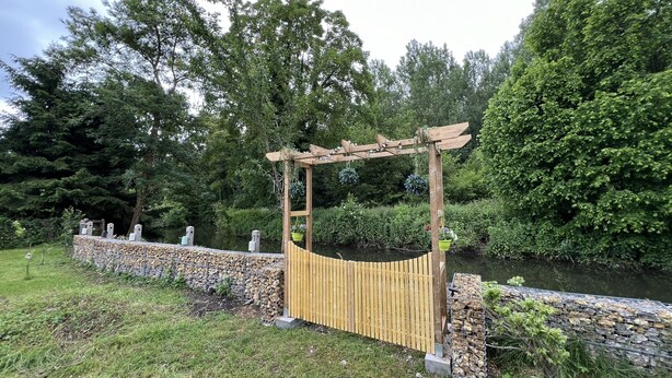 Een houten pergola met een gebogen dak, een stenen muur en een gazon ervoor.