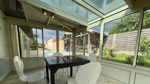 Een oranjerie met glazen dak, een eettafel en twee stoelen.