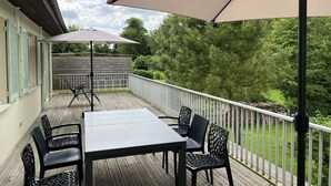 Een terras met een tafel en stoelen, een pergola met zonnescherm, en uitzicht op bomen en een houten hek.