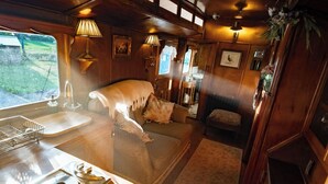 L’intérieur d’un chalet accueillant, avec un lit, une petite table avec des assiettes, un évier et une fenêtre donnant sur un paysage verdoyant.