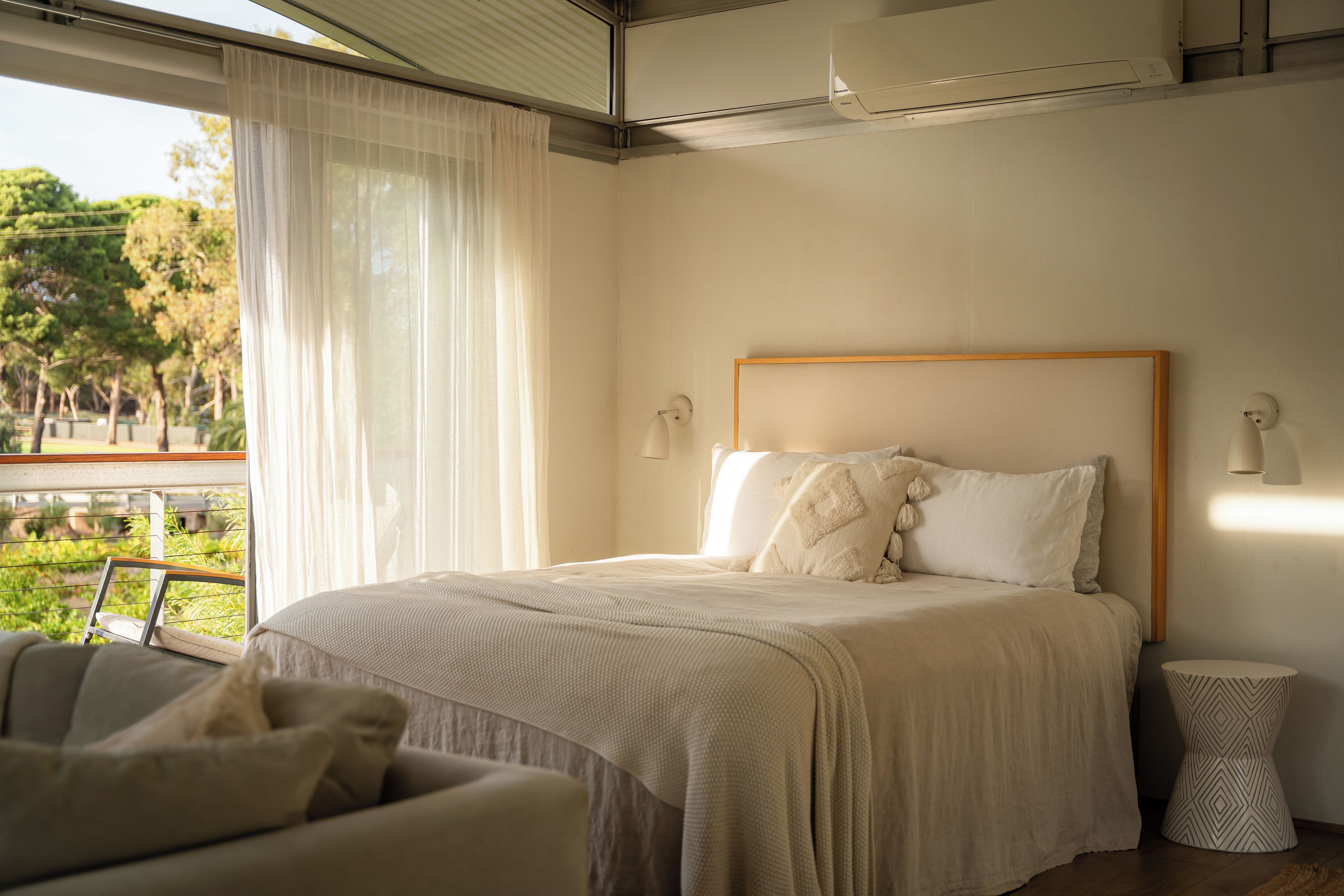 A bedroom with a bed, a chair, a bedside table, and a view of greenery outside.