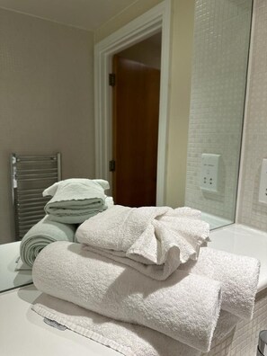 A bathroom with a stack of white towels on a counter, a towel rack, and a wooden door in the background.