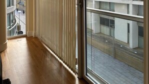 Un apartamento moderno con un amplio ventanal corredero que da a un balcón, suelo de madera y vistas a un paisaje urbano.
