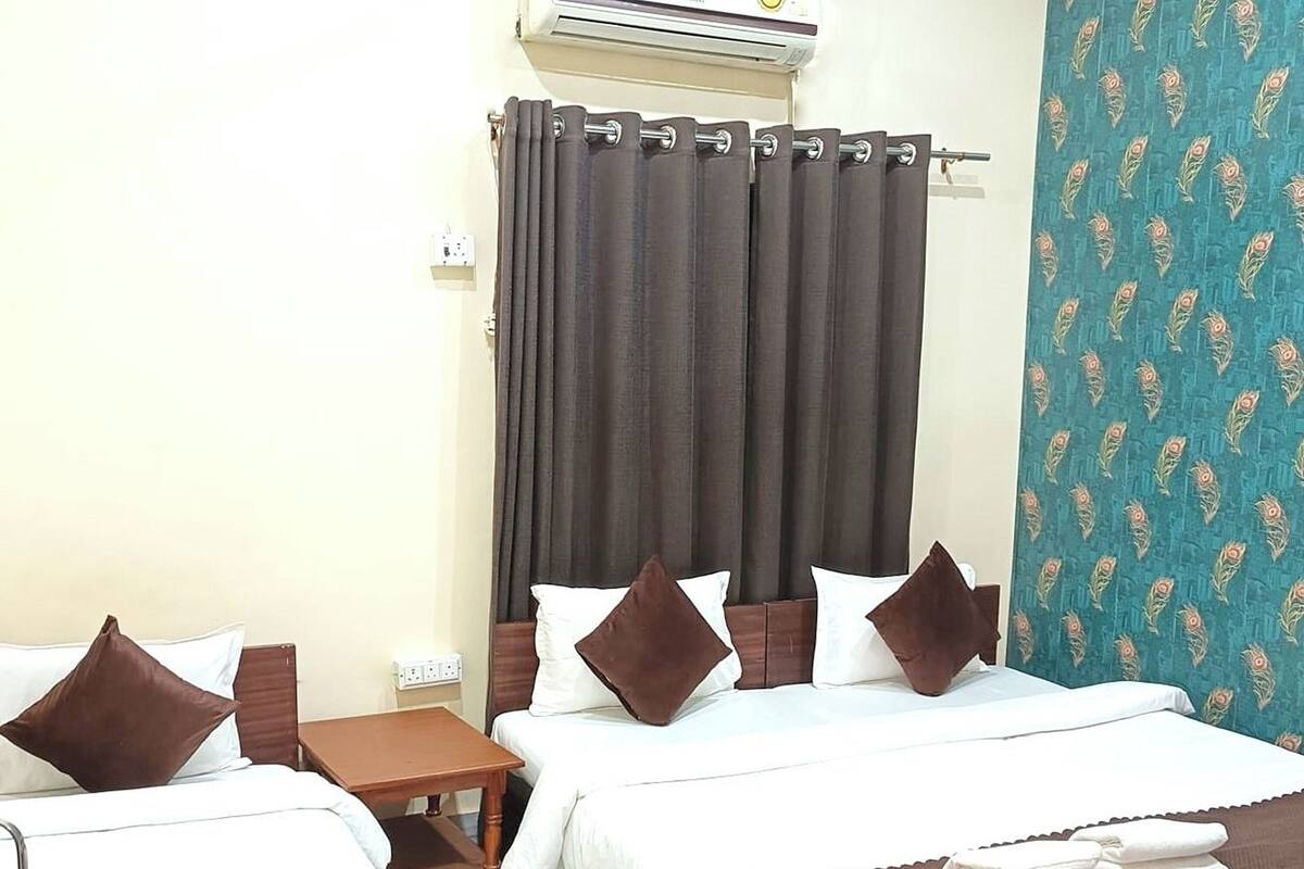 A hotel room with two beds, a small wooden table, a curtain, and a patterned wall.
