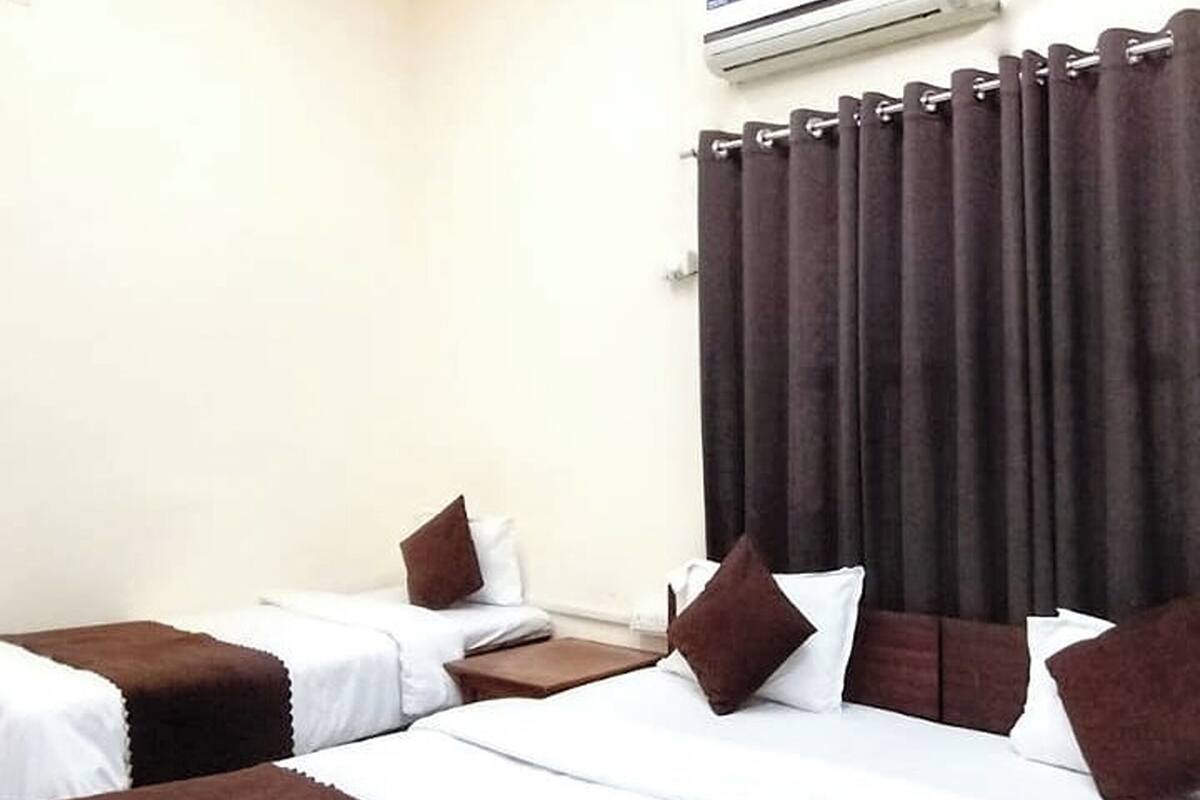 A hotel room with two beds, a ceiling fan, an air conditioning unit, and a window with curtains.
