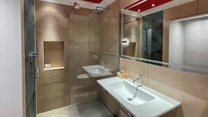 Ein modernes Badezimmer mit einer gläsernen Duschkabine, einem weißen Waschbecken und einem großen Spiegel.