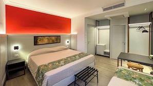 Ein modernes Hotelzimmer mit Bett, Nachttisch, Bank und Schreibtisch mit Stuhl.