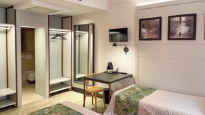 Ein Hotelzimmer mit Bett, Schreibtisch mit Stuhl, Kleiderschrank, Spiegel, Fernseher und zwei gerahmten Bildern an der Wand.