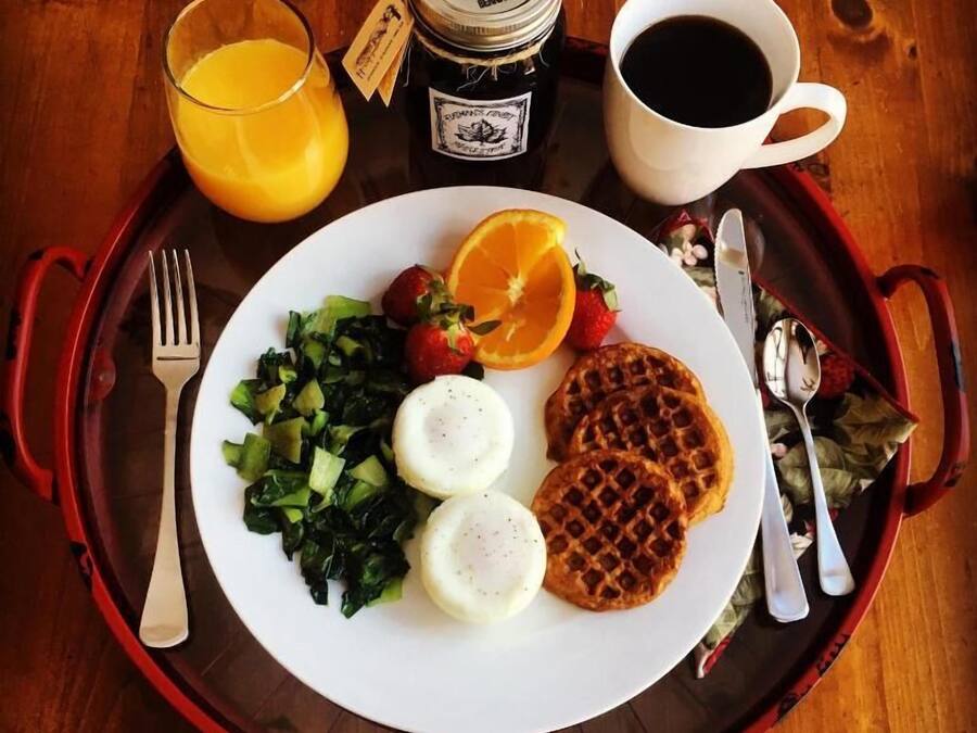 A tray with a plate of food including greens, strawberries, an orange slice, waffles, and a glass of orange juice.