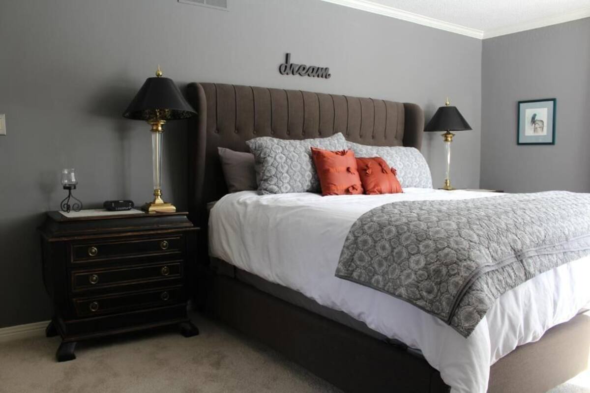 Un dormitorio con una cama grande, dos mesitas de noche, un aparador y una lámpara de pared.
