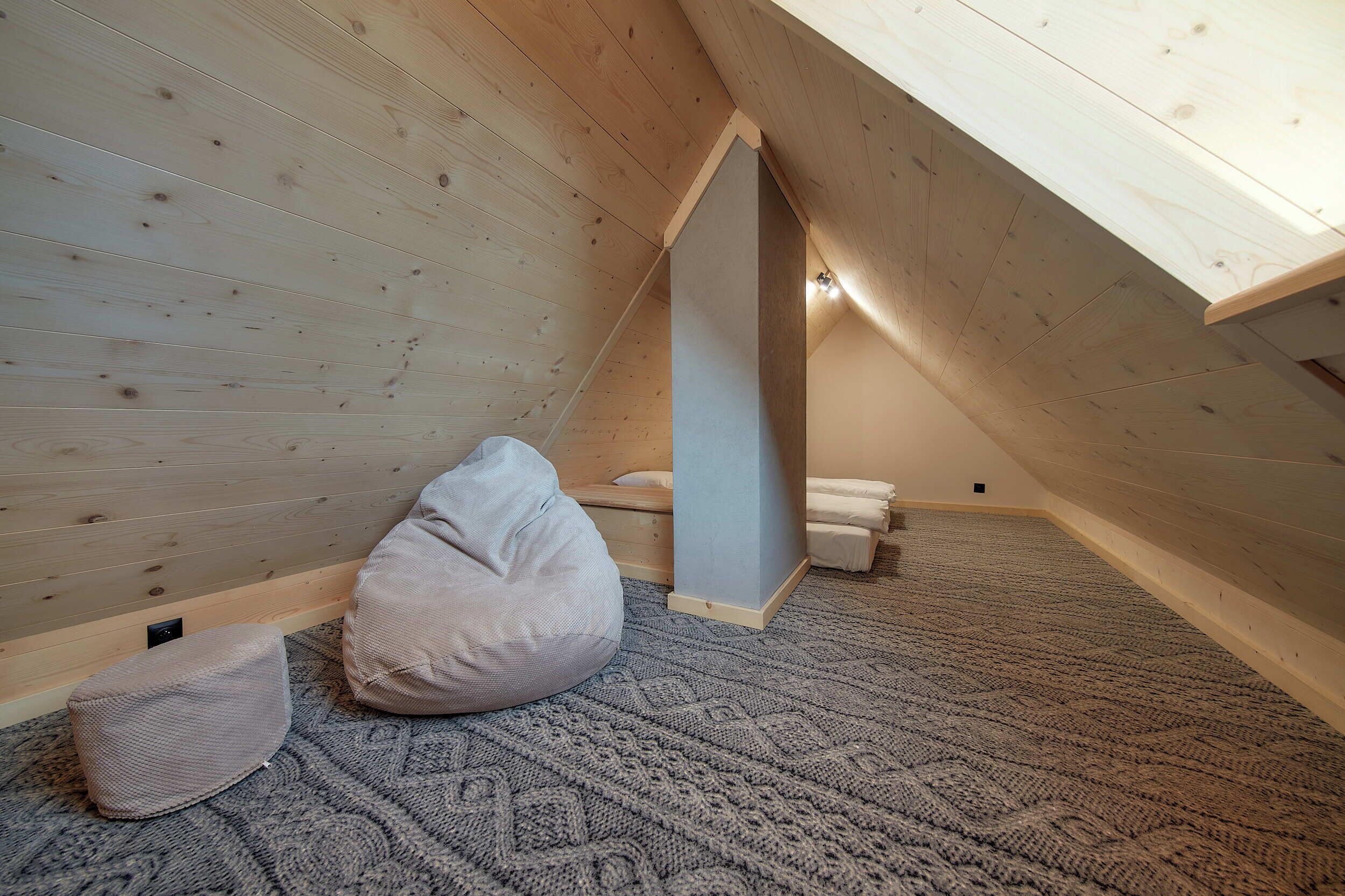 A cozy attic bedroom with wooden walls, a slanted ceiling, and a knitted rug.