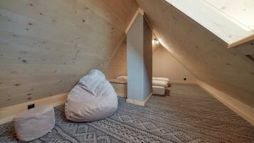 A cozy attic bedroom with wooden walls, a slanted ceiling, and a knitted rug.