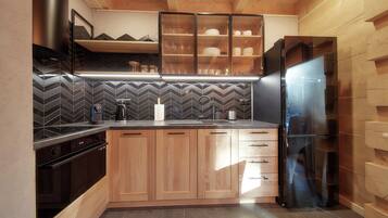 A compact kitchen with wooden cabinets, a built-in oven, a stainless steel refrigerator, and a herringbone tile backsplash.