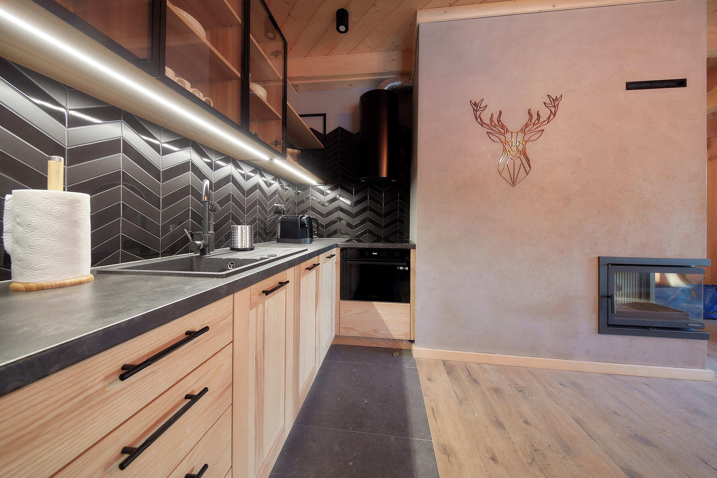A modern kitchen with a herringbone tile backsplash, wooden cabinets, and a built-in oven.