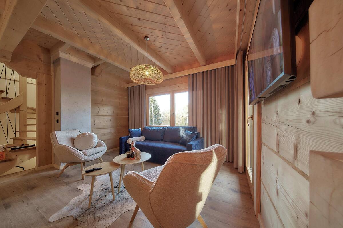 Un interior acogedor de madera con un sofá, dos sillones, una mesita y una lámpara colgante.