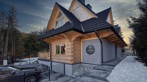 A log cabin with a steeply pitched roof, a wooden exterior, and a sign indicating it is a Tatra Wood House.