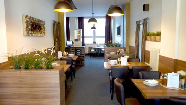 A restaurant with wooden tables and chairs, potted plants, and pendant lighting. - Hotel Veronika (Ostrava)