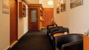 A hotel lobby with a carpeted floor, wooden doors, black leather seating, and wall-mounted artwork. - Hotel Veronika (Ostrava)