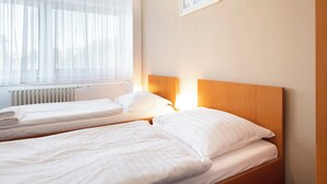 A hotel room with two single beds, a window with sheer curtains, a radiator, and a framed picture on the wall. - Hotel Veronika (Ostrava)