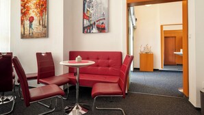 A modern hotel lobby with a red sofa, matching chairs, a small round table, and two paintings on the walls. - Hotel Veronika (Ostrava)
