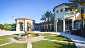 A courtyard with a fountain, palm trees, and a building with arches. - CG 1407 Rolling Fairway Rolling Skies Poolside Cinema Spa Near Disney (Davenport)