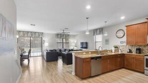 A modern kitchen with wooden cabinets, a central island, and a dining area with a sofa. - CG 1407 Rolling Fairway Rolling Skies Poolside Cinema Spa Near Disney (Davenport)