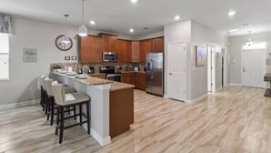 A modern kitchen with wooden cabinets, a stainless steel refrigerator, and a bar area with stools. - CG 1407 Rolling Fairway Rolling Skies Poolside Cinema Spa Near Disney (Davenport)