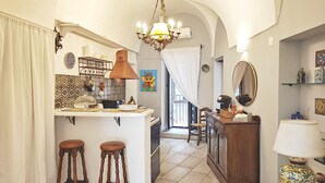 A kitchen with a central island, two wooden stools, a chandelier, and a dining area with a wooden table and chairs.