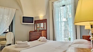 A hotel room with a bed, a desk, a TV, a dresser, and a window with curtains.