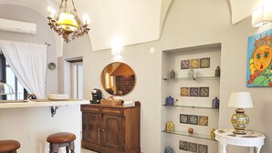 A well-lit room with a wooden cabinet, a mirror, a shelf with decorative items, and a small table with a lamp.