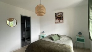 A bedroom with a bed, two bedside tables, a hanging light fixture, a mirror, and a door leading to another room.