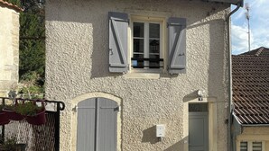 A two-story building with a textured facade, a small window with shutters, and a door with a number plaque.