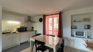 A compact kitchen with a dining table, chairs, a microwave, a kettle, and a clock on the wall.