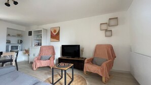 A living room with two armchairs, a TV, a small table, and a kitchen area with a microwave and toaster.