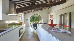 A modern kitchen with a central island, stainless steel appliances, and a view through an arched window to the outdoors. - Podere Gabbiano, Castellina in Chianti, Siena and Chianti (Castellina in Chianti)